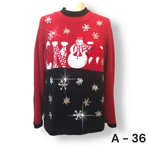 May include: Red and black Christmas sweater with a snowman and the word "SNOW" appliqued on the front. The snowman has a red hat and scarf. The sweater is decorated with snowflakes.