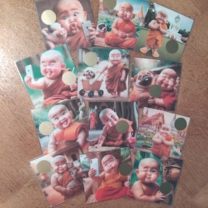May include: A selection of square cards displaying images of a smiling, bald figure in orange robes, resembling a Buddhist monk. The cards show the figure with animals and taking selfies with a smartphone. Each card has a gold circle.