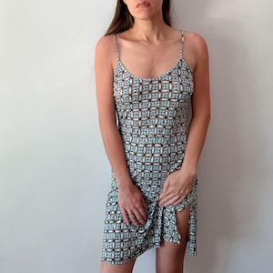 May include: A sleeveless knee-length dress featuring a repeating geometric pattern in shades of light blue, dark brown, and white. The garment has thin spaghetti straps, a scoop neckline, and a straight-cut hemline with a side slit detail.