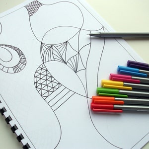 Può includere: Un quaderno a spirale con arte lineare astratta, accompagnato da un set di penne a punta fine colorate. Le penne hanno cappucci di vari colori, tra cui rosso, arancione, giallo, verde, blu e viola. Una penna è appoggiata sulla pagina.