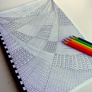 Peut inclure: Un carnet &agrave; spirales avec un motif g&eacute;om&eacute;trique noir et blanc. Un ensemble de six crayons de couleur rouge, orange, jaune, vert, bleu et turquoise est dispos&eacute; sur le c&ocirc;t&eacute; droit du carnet. Les crayons sont taill&eacute;s.