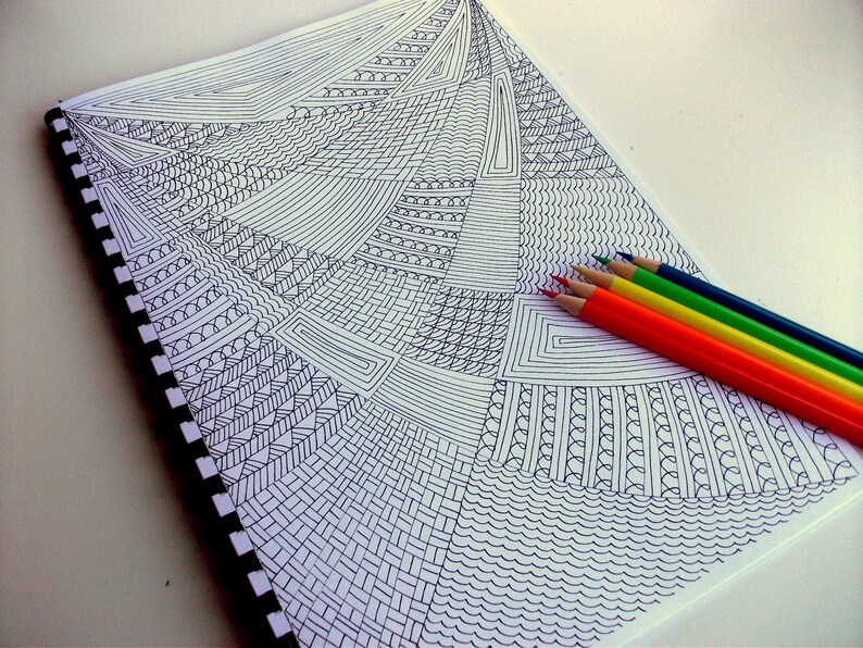 Peut inclure: Un carnet &agrave; spirales avec un motif g&eacute;om&eacute;trique noir et blanc. Un ensemble de six crayons de couleur rouge, orange, jaune, vert, bleu et turquoise est dispos&eacute; sur le c&ocirc;t&eacute; droit du carnet. Les crayons sont taill&eacute;s.