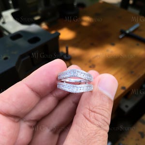 Peut inclure: Une protection de bague en argent avec un design incurvé, incrustée de petits pierres précieuses scintillantes. La protection de bague est tenue dans une main, mettant en valeur ses détails complexes et son savoir-faire. L'arrière-plan est flou.