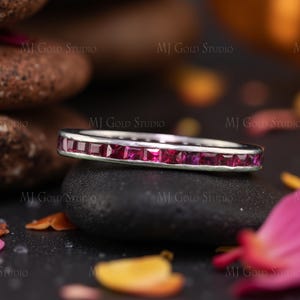 Könnte beinhalten: Ein silberner Ring mit einer Reihe quadratisch geschliffener, leuchtend roter Edelsteine. Der Ring ist vor einem dunklen Hintergrund platziert, mit dem Text "MJ Gold Studio" sichtbar. Der Ring ist ein Schmuckstück.