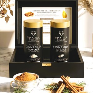 May include: A black box with gold accents holds two black and gold spice containers labeled "VP Aura Ceylon Cinnamon Powder" and "Cinnamon Sticks." A teacup filled with cinnamon powder and cinnamon sticks are in the foreground.