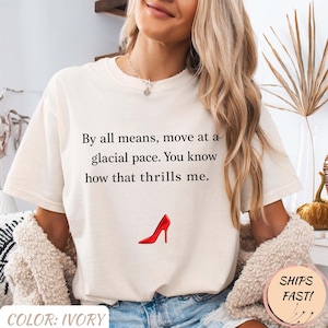May include: Ivory t-shirt featuring the text "By all means, move at a glacial pace. You know how that thrills me." and a red high heel graphic. The shirt is a casual style.