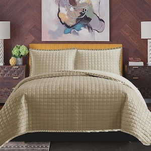 May include: A beige quilted bedspread and pillow set. The bedding has a grid pattern and a decorative trim. The bed is made up with two pillows and a comforter. The headboard is yellow and the background is a dark wood.