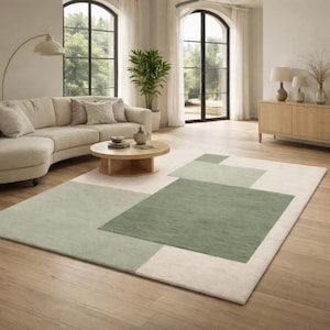 May include: A rectangular area rug with a geometric design in shades of green and cream. The rug features large, overlapping squares and rectangles, creating a modern and stylish look. The rug is placed on a hardwood floor in a living room setting.