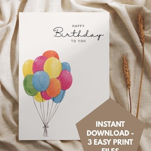 Könnte beinhalten: Eine weiße Grußkarte mit einer Aquarellillustration eines Bündels bunter Luftballons in Rot, Gelb, Blau, Grün und Pink, mit schwarzen Schnüren, die unten zusammengebunden sind, und dem in Schwarz gedruckten Text Happy Birthday TO YOU.