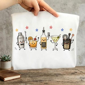 May include: A white t-shirt featuring a graphic of five anthropomorphic bar tools and cocktails with smiling faces. The design includes a shaker, an old fashioned, a liquor bottle labelled 'GOOD DRINKS GOOD TIMES', a martini, and a mixing glass labelled 'SHAKE STIR ENJOY'.