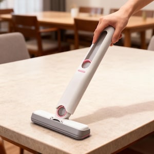 Puede incluir: Una herramienta de limpieza gris claro y blanca con detalles en rosa se sostiene sobre una mesa. La herramienta tiene un cabezal rectangular y un mango largo. El mango tiene un diseño circular rosa. El cabezal es gris y blanco con un borde rosa.