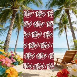 Puede incluir: Una toalla de playa roja con un patrón repetido del logotipo blanco "Dr Pepper". La toalla está colgada de un tendedero entre dos palmeras en una playa soleada. Una silla de playa de madera y flores están en el fondo.