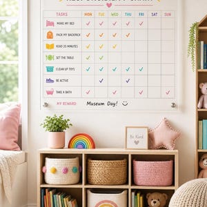 May include: A clear acrylic responsibility chart titled OLIVIA'S RESPONSIBILITY CHART with a grid of tasks including make my bed, pack my backpack, read 20 minutes, set the table, clean up toys, be active, and take a bath with checkmarks.