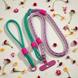 Könnte beinhalten: Zwei Handy-Lanyards, eines mit floralem Muster und das andere türkisgrün, beide mit rosa Akzenten. Die Lanyards haben einen rosa Handyhalter. Der Hintergrund ist weiß mit verstreuten Blumen.