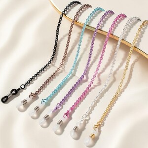 Peut inclure: Une collection de sept chaînes de lunettes de différentes couleurs, dont le noir, le bronze, le bleu clair, le violet, le rose, l'argent et l'or. Chaque chaîne présente un design de maillons délicats et des boucles en caoutchouc transparentes.
