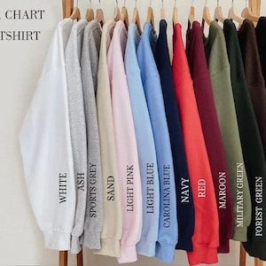 May include: A color chart for sweatshirts featuring a row of long-sleeved crewneck garments in various colors including white, ash, sports grey, sand, light pink, light blue, carolina blue, navy, red, maroon, military green, forest green, dark chocolate, and black.