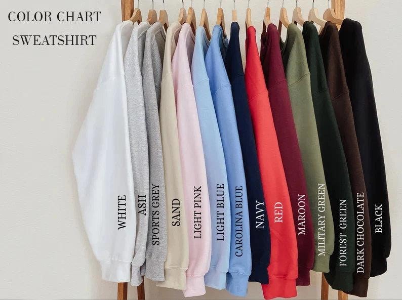 May include: A color chart for sweatshirts featuring a row of long-sleeved crewneck garments in various colors including white, ash, sports grey, sand, light pink, light blue, carolina blue, navy, red, maroon, military green, forest green, dark chocolate, and black.
