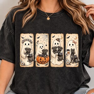 May include: A charcoal grey mineral-washed t-shirt featuring four rectangular panels with illustrations of white ghosts and black Cane Corso puppies. The designs include ghosts with flowers, a pumpkin, a hat, and a coffee cup, all wearing skeleton outfits.