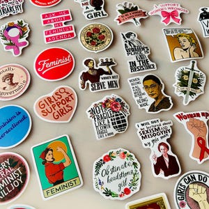 Könnte beinhalten: Eine Sammlung verschiedener Vinyl-Aufkleber mit diversen feministischen Illustrationen, Slogans und Porträts. Die Aufkleber zeigen unterschiedliche Designs, darunter Texte, florale Motive, historische Persönlichkeiten und grafische Symbole in einer Vielzahl von Farben.