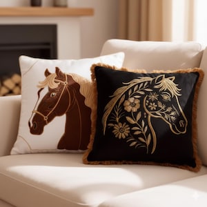 Op de afbeelding: Twee decoratieve sierkussens met paardenontwerpen. Eén kussen is wit met een bruine paardenkop, de andere is zwart met een gouden paardenkop en bloemmotieven. Beide kussens liggen op een crèmekleurige bank.
