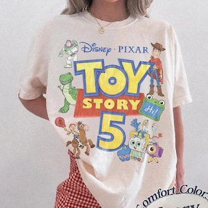 Puede incluir: Una camiseta de color marfil con un estampado gr&aacute;fico que incluye el texto Disney Pixar Toy Story 5. El dise&ntilde;o presenta ilustraciones de Buzz Lightyear, Woody, Rex, Jessie, Bullseye y otros personajes. La camiseta tiene cuello redondo y mangas cortas.