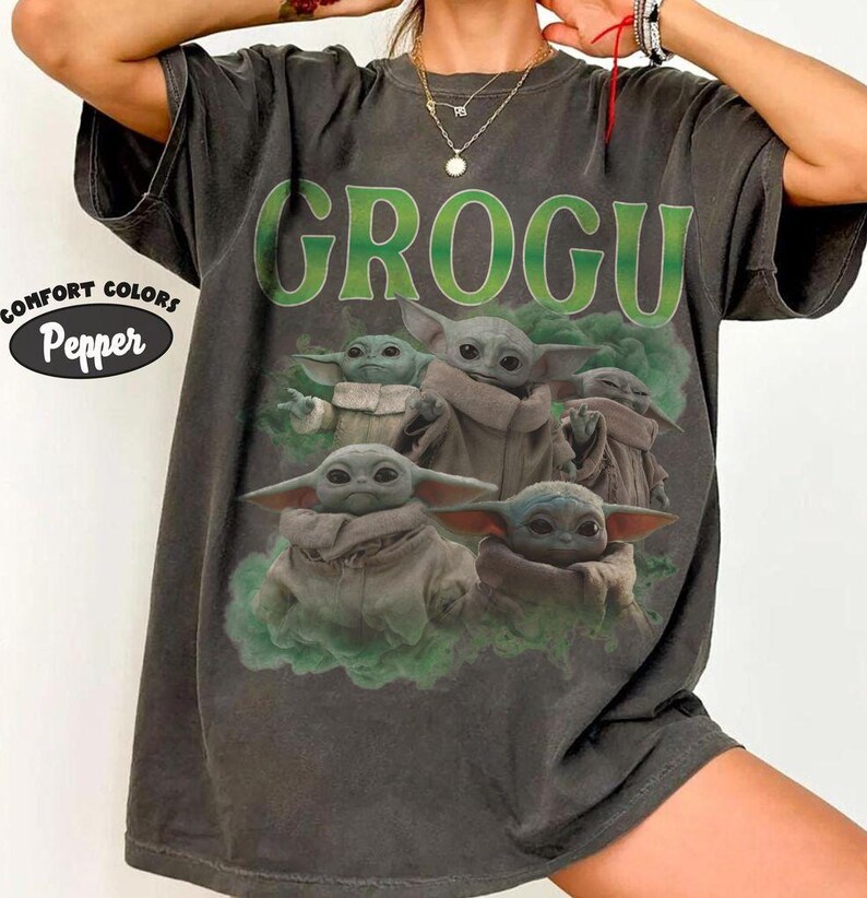 May include: A charcoal gray short-sleeve t-shirt featuring a graphic print of multiple Grogu characters surrounded by green smoke. The text GROGU is printed in large green letters above the characters. A Comfort Colors Pepper label is visible.