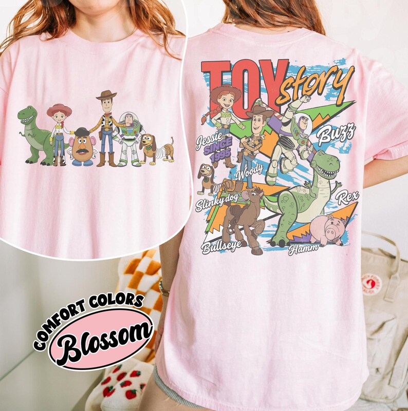Może przedstawiać: Jasnor&oacute;żowa koszulka z grafiką postaci z Toy Story, w tym Chudego, Buzz'a Astrala i Rexa. Tył koszulki przedstawia logo Toy Story i więcej postaci. Koszulka ma r&oacute;wnież napisy "Comfort Colors" i "Blossom".