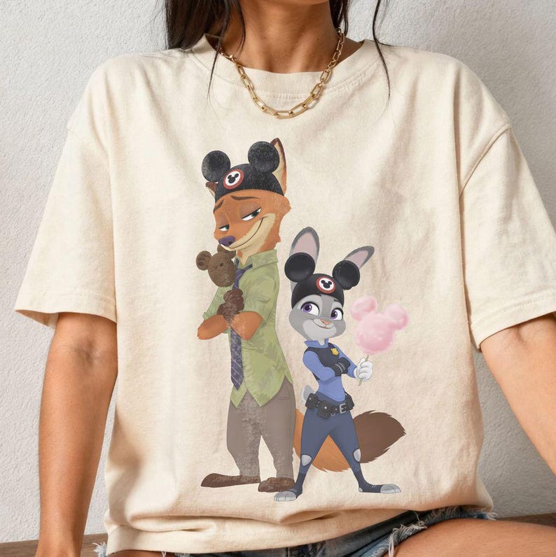 Pu&ograve; includere: T-shirt color crema con un'illustrazione di due personaggi di Zootropolis. Uno &egrave; una volpe con un cappello con orecchie da topo e un orsacchiotto. L'altro &egrave; un coniglio in uniforme da poliziotto, con zucchero filato rosa.