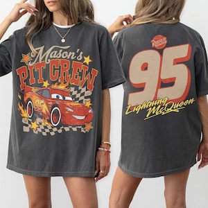 Op de afbeelding: Een antracietgrijs t-shirt met korte mouwen met een afbeelding van een rode raceauto met vlammen en de tekst Mason's PIT CREW op de voorkant. De achterkant toont het nummer 95 in een groot beige lettertype met de tekst Lightning McQueen eronder.