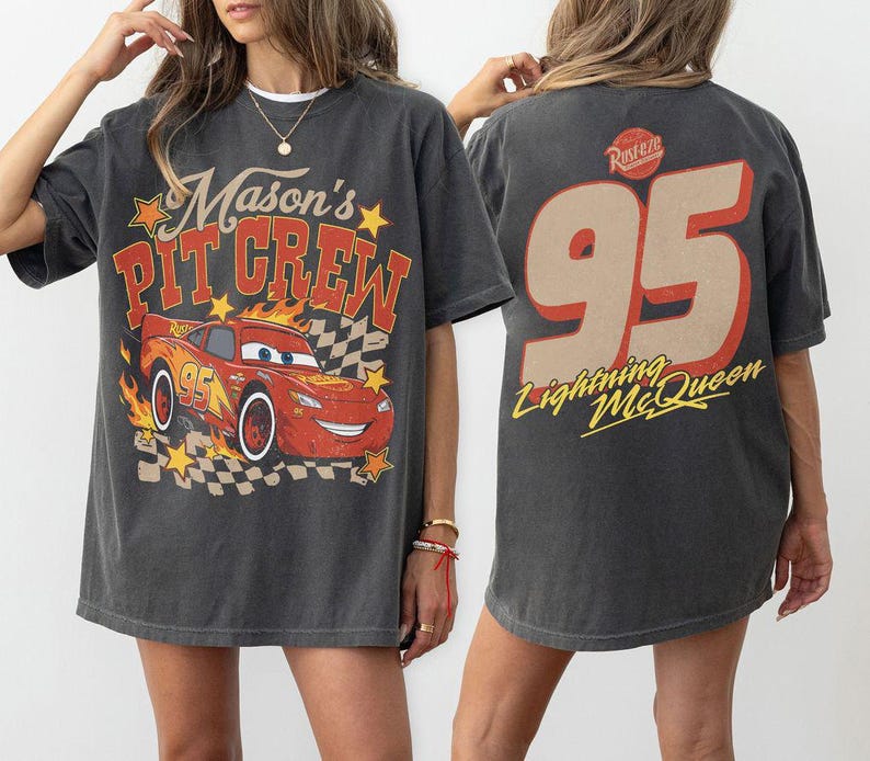 Op de afbeelding: Een antracietgrijs t-shirt met korte mouwen met een afbeelding van een rode raceauto met vlammen en de tekst Mason's PIT CREW op de voorkant. De achterkant toont het nummer 95 in een groot beige lettertype met de tekst Lightning McQueen eronder.