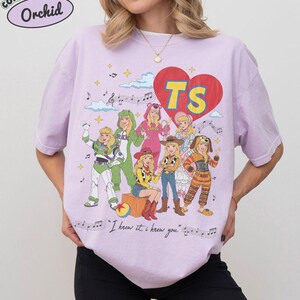 Puede incluir: Una camiseta de color morado claro con un estampado gr&aacute;fico de siete personajes disfrazados, un gran coraz&oacute;n rojo con las letras amarillas TS, notas musicales y el texto I knew it, i knew you en una fuente cursiva.