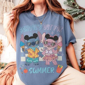 May include: A blue t-shirt with the text "SCHOOL'S OUT FOR SUMMER" and a cartoon graphic of two characters holding ice cream cones. One character is blue and the other is pink. The shirt has a checkered background.