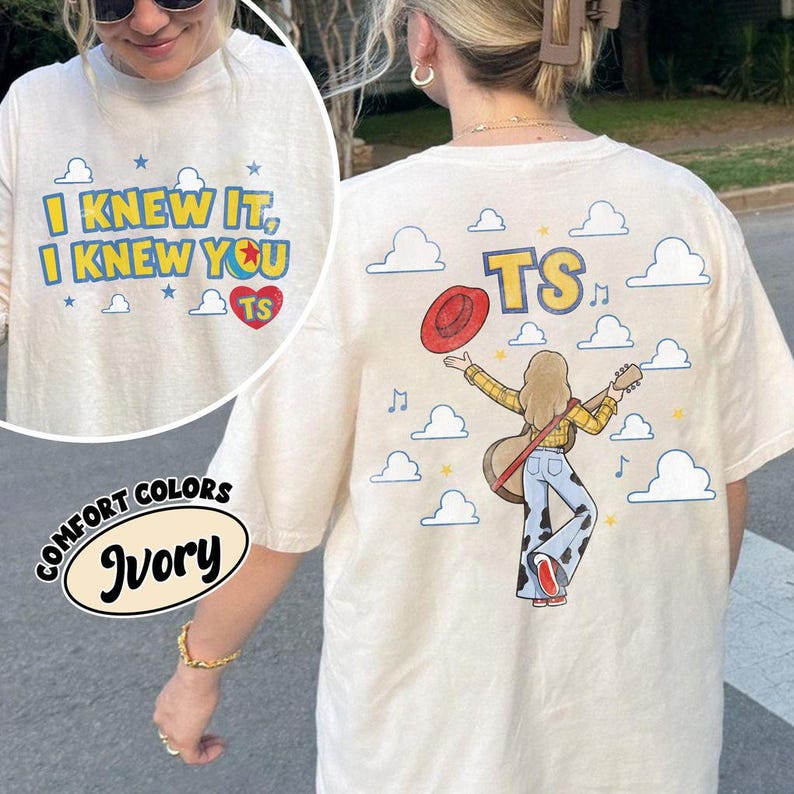 May include: An ivory t-shirt featuring a front graphic with the text I KNEW IT, I KNEW YOU TS and a red heart. The back graphic shows a person in a yellow plaid shirt and cow-print trousers holding a guitar and red hat, with the text TS and clouds.