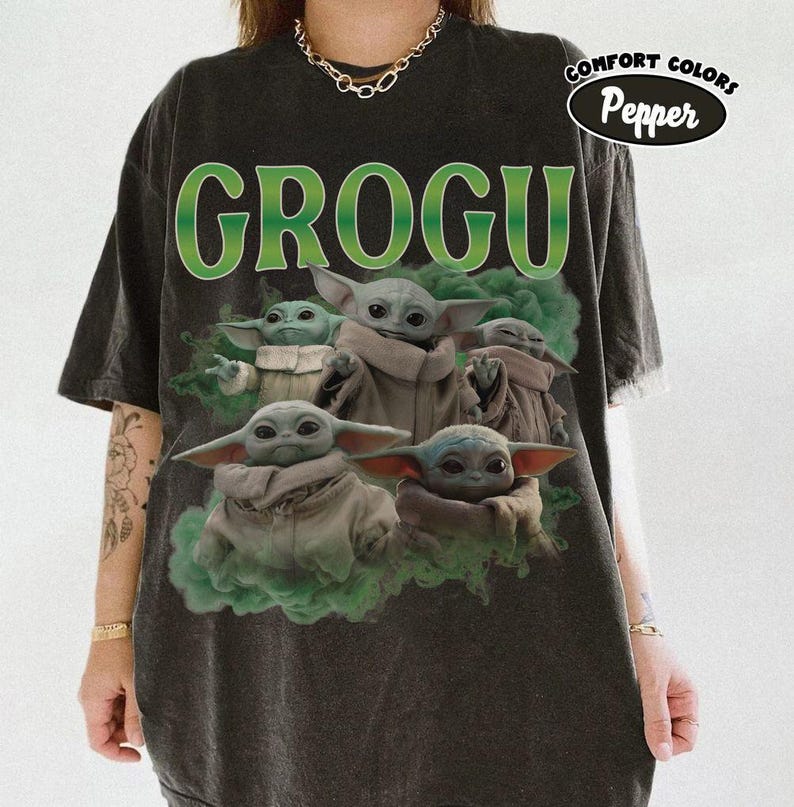 May include: A charcoal gray short-sleeve t-shirt featuring the green text GROGU at the top. The graphic displays multiple illustrations of the character Grogu surrounded by green smoke. A small circular logo in the corner reads COMFORT COLORS Pepper.