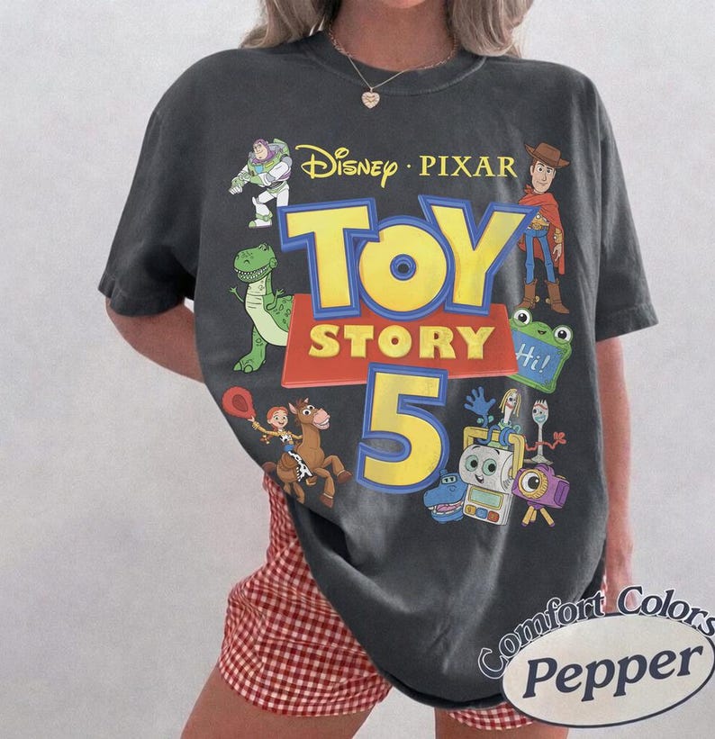 Puede incluir: Una camiseta de manga corta gris carb&oacute;n con un estampado gr&aacute;fico que incluye el texto Disney Pixar Toy Story 5. El dise&ntilde;o presenta ilustraciones de Buzz Lightyear, Woody, Rex, Jessie, Bullseye, Forky y otros personajes en colores vivos.