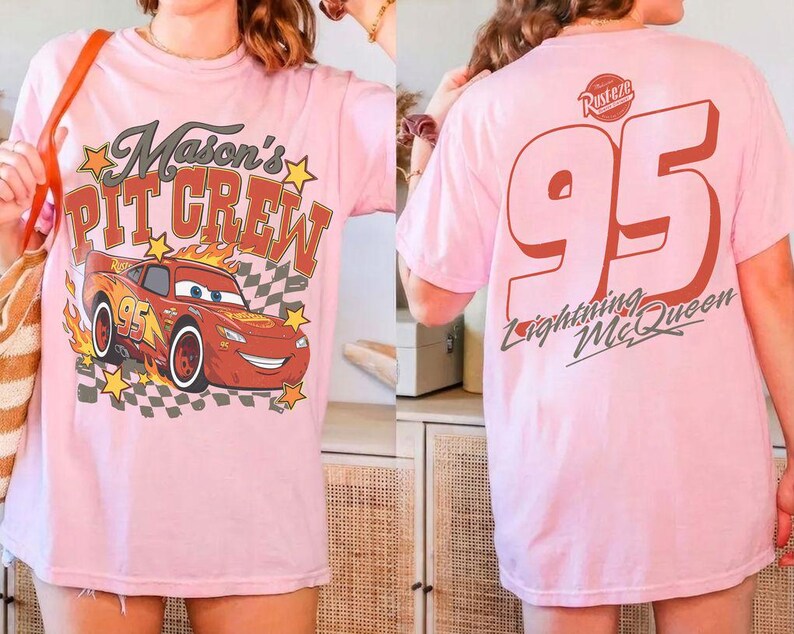 Op de afbeelding: Een lichtroze t-shirt met een afbeelding op de voorkant van een rode raceauto met vlammen, een dambordpatroon, gele sterren en de tekst Mason's PIT CREW. De achterkant toont het nummer 95, het Rust-eze logo en de tekst Lightning McQueen.