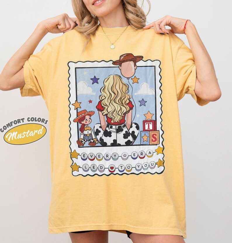 May include: A mustard yellow t-shirt featuring a graphic print of a blonde person seen from behind, a small cowgirl doll, a cowboy hat balloon, and alphabet blocks. The text reads "EVERY ERA LED TO YOU" inside a decorative postage stamp border.