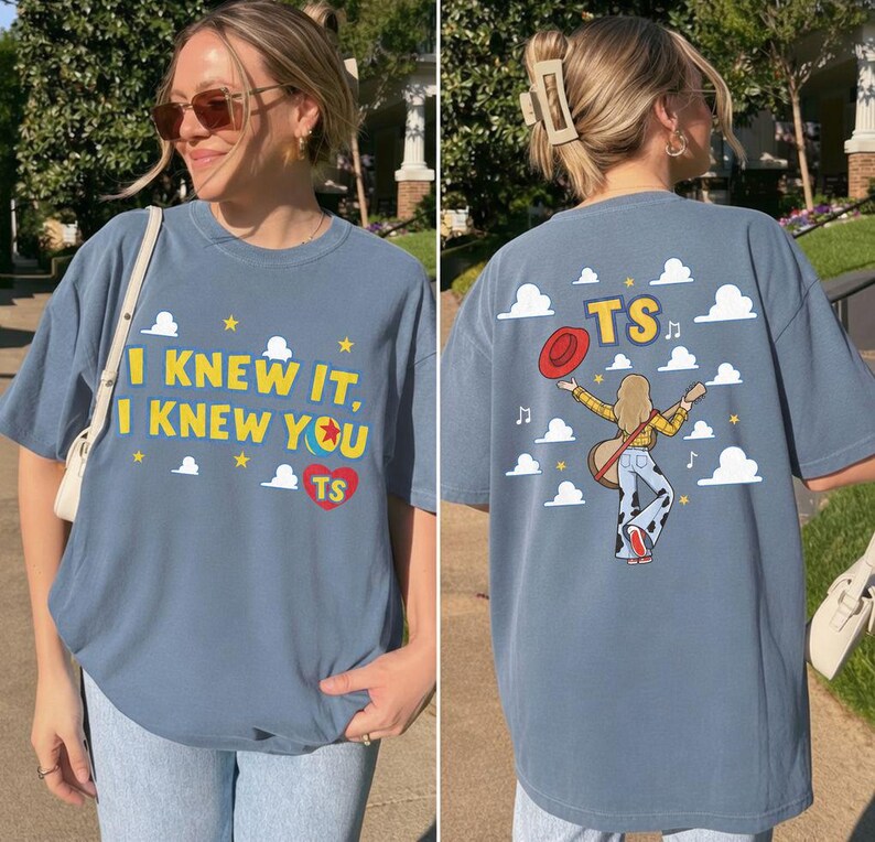 May include: A blue t-shirt featuring a graphic design. The front displays the text I KNEW IT, I KNEW YOU with a ball icon and a red heart containing TS. The back shows a person with a guitar, a red hat, and the text TS amidst white clouds.