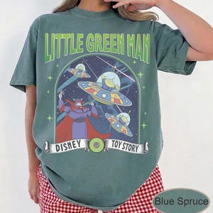 May include: A blue spruce t-shirt with a Disney Toy Story graphic. The design features the text "Little Green Man" above a scene with aliens in flying saucers and the character Zurg.