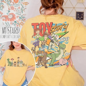Może przedstawiać: Musztardowa koszulka comfort colors z grafiką postaci z Toy Story. Projekt zawiera Woody'ego, Buzz Lightyeara, Jessie, Rexa i Hamma. Tekst "Toy Story" jest wydrukowany na g&oacute;rze.