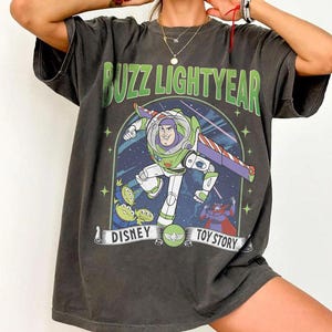 May include: Dark grey t-shirt featuring Buzz Lightyear from Disney's Toy Story. The graphic includes Buzz in his spacesuit, aliens, and the text "Buzz Lightyear" and "Disney Toy Story".