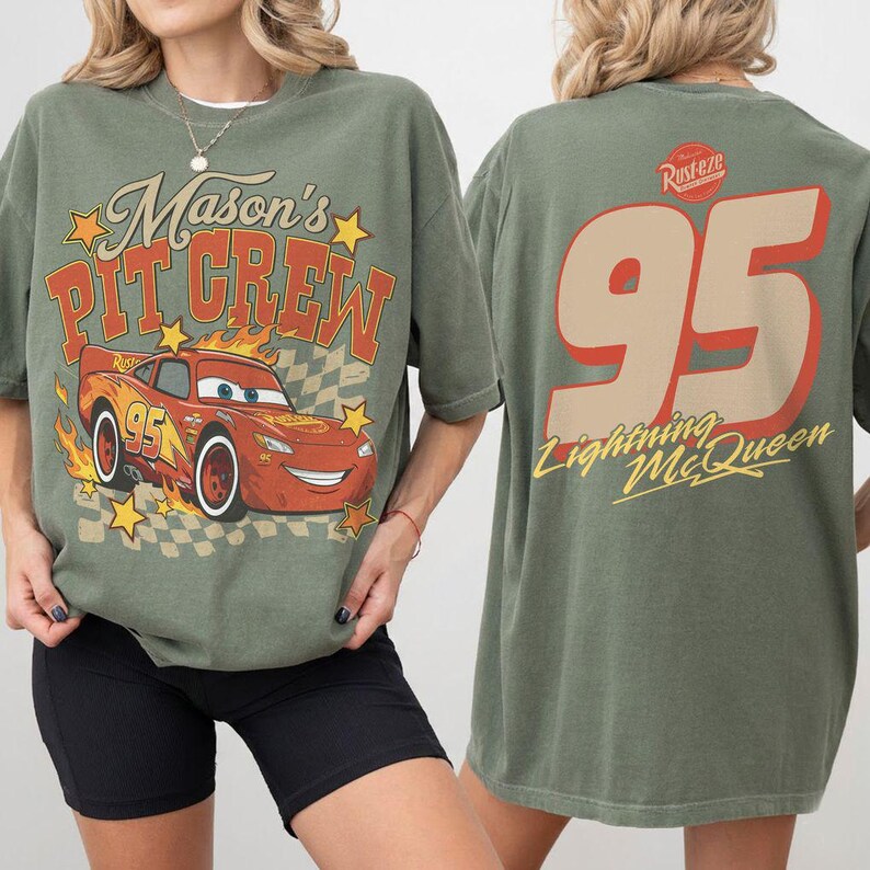 Op de afbeelding: Een olijfgroen t-shirt met een afbeelding van een rode raceauto en de tekst Mason's Pit Crew op de voorkant. De achterkant toont het nummer 95 in een groot beige lettertype met de tekst Lightning McQueen en een rood-wit Rust-eze logo.