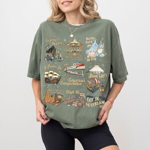 K&ouml;nnte beinhalten: Olivgr&uuml;nes T-Shirt mit Vintage-Design, das Themenpark-Illustrationen und S&auml;tze wie "Foolish Mortals" und "Off to Neverland" zeigt. Das Shirt zeigt ein Karussell, ein Piratenschiff und eine Rakete, mit dem Jahr 1967.