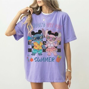 May include: A lilac-colored t-shirt featuring a cartoon illustration of Stitch and Angel holding ice cream cones. The text "SCHOOL'S OUT FOR SUMMER" is printed above the characters. The shirt has a relaxed fit.