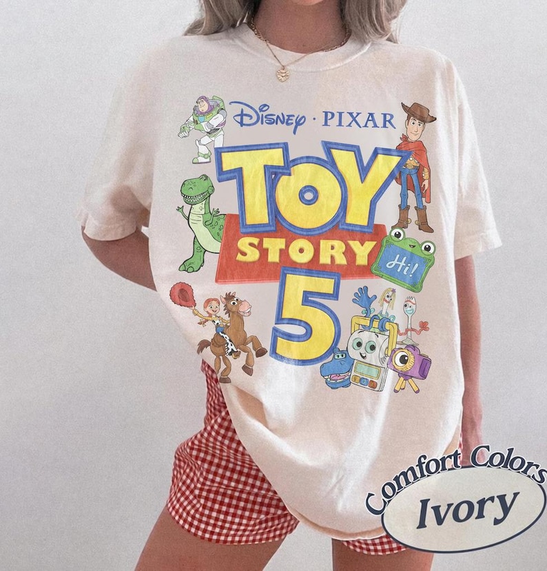 Puede incluir: Una camiseta de color marfil con un estampado gr&aacute;fico que incluye el texto Disney Pixar Toy Story 5. El dise&ntilde;o presenta ilustraciones de Buzz Lightyear, Woody, Rex, Jessie, Bullseye y otros personajes. La camiseta tiene cuello redondo y mangas cortas.