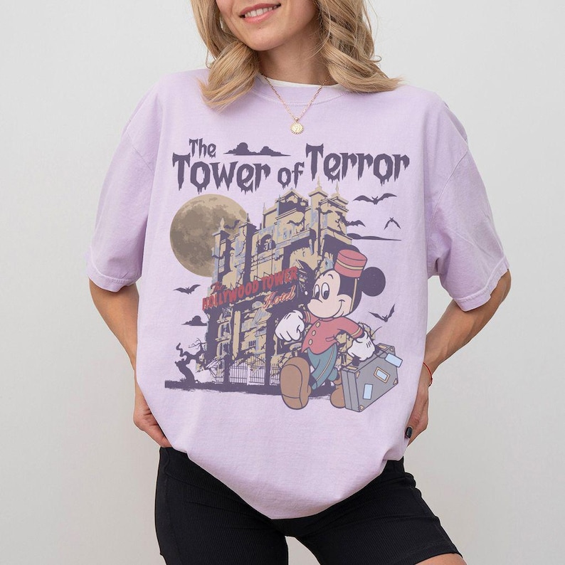 Puede incluir: Camiseta lila claro con un dise&ntilde;o de Mickey Mouse frente a la Torre del Terror. El texto "The Tower of Terror" est&aacute; sobre la imagen. El dise&ntilde;o incluye una luna llena y murci&eacute;lagos.