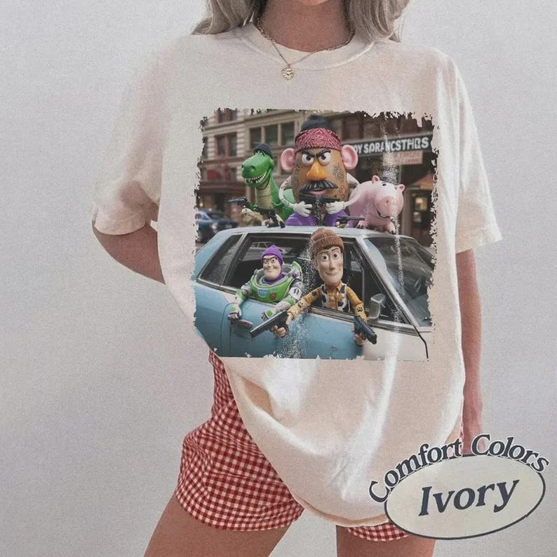Puede incluir: Una camiseta de manga corta color marfil con un estampado gr&aacute;fico de personajes de Toy Story, incluidos Woody, Buzz Lightyear, el Sr. Patata, Rex y Hamm en un coche. El estampado tiene un borde desgastado e incluye el texto Toy Story.