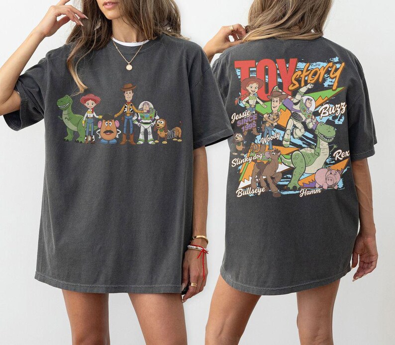 Może przedstawiać: Ciemnoszara koszulka z kolorową grafiką postaci z Toy Story, w tym Chudego i Buzz'a Astrala. Prz&oacute;d koszulki przedstawia postacie, a tył logo Toy Story i więcej postaci. Zabawny, codzienny t-shirt.