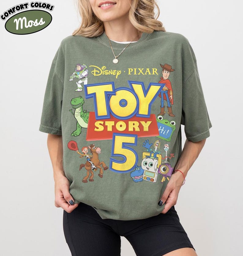 Puede incluir: Una camiseta de manga corta color verde musgo con un estampado gr&aacute;fico que incluye el texto Disney Pixar Toy Story 5. El dise&ntilde;o presenta ilustraciones de Buzz Lightyear, Woody, Rex, Jessie sobre Perdig&oacute;n, Forky y otros personajes en amarillo, azul y rojo.