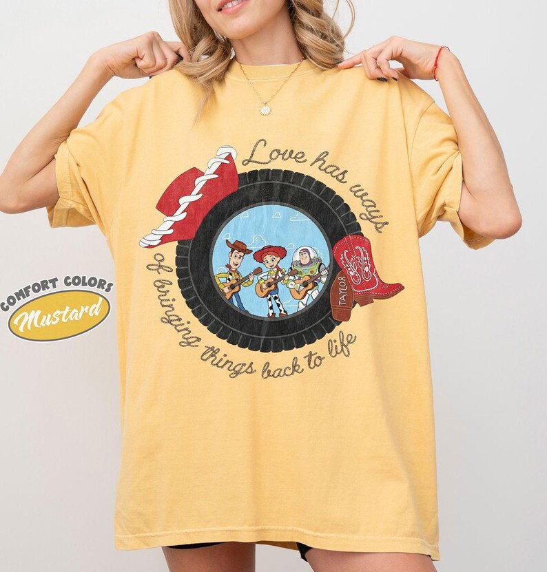 May include: A mustard yellow t-shirt featuring a graphic of a black tire surrounding a scene with three cartoon characters playing guitars. The text reads, Love has ways of bringing things back to life. A red cowboy hat and a red cowboy boot are included.